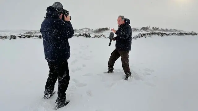 A cameraman and report in a field covered with deep snow, filming a news report
