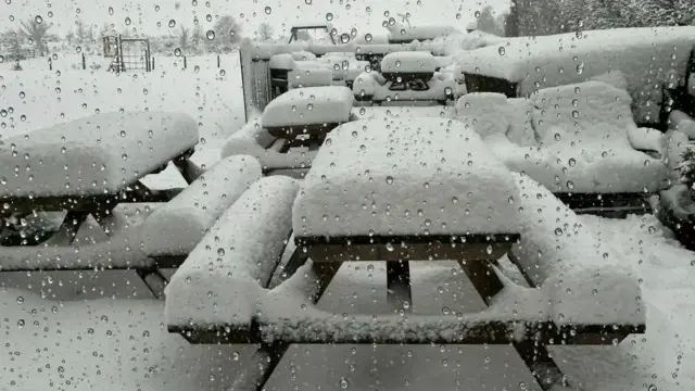 Several inches of snow cover picnic benches.