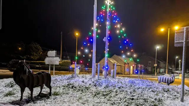 A roundabout covered in snow. Christmas lights illuminate the scene