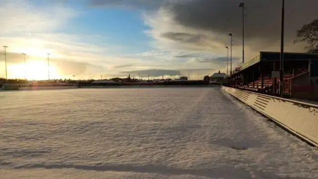 A snow-covered football pitch as the sun rises.