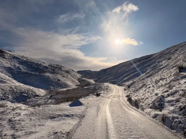 A rural road with mountains on either side covered in snow.