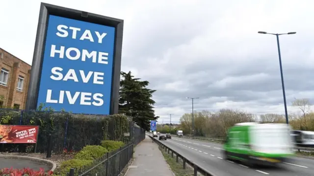 A public service sign reading "Stay Home, Save Lives" is displayed on a road