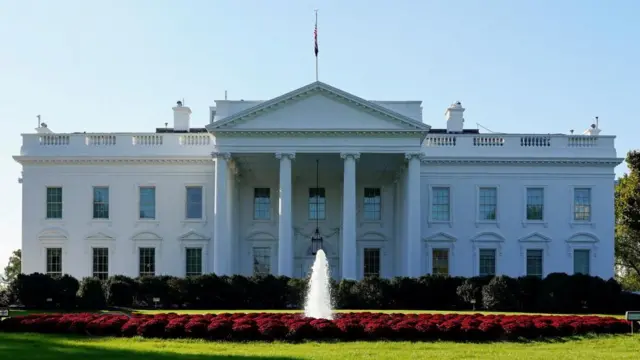 The north side of the White House on a sunny day with the fountain and red flowers visible on the lawn