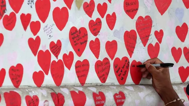 A person writes a message on the National Covid Memorial Wall