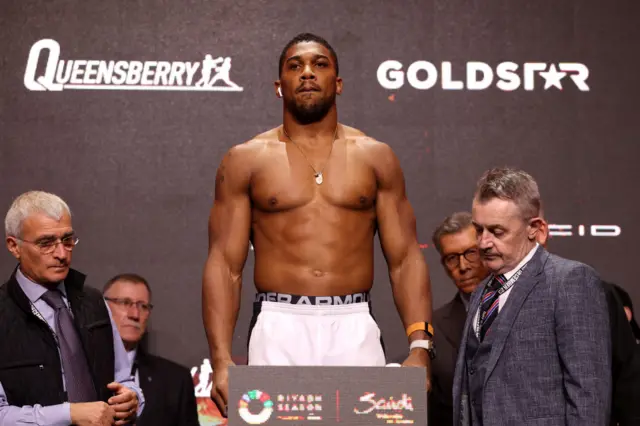 Anthony Joshua is shirtless and standing on scales