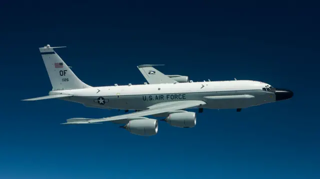 A grey and white RC-135 surveillance aircraft. It's a four-engined jet that has a large black nosecone