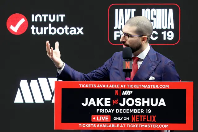 Ariel Helwani stands behind a podium and holds up his arm