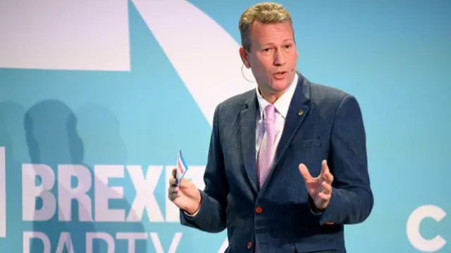 Nathan Gill in a blue suit in front of a background reading Brexit Party