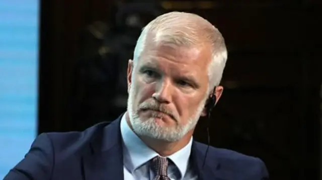 Alistair Carns seated at a conference listening to moderator