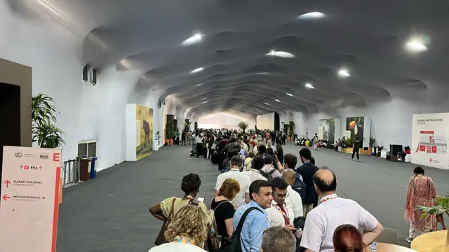 Long queue of people in a grey conference hall, with artificial lighting