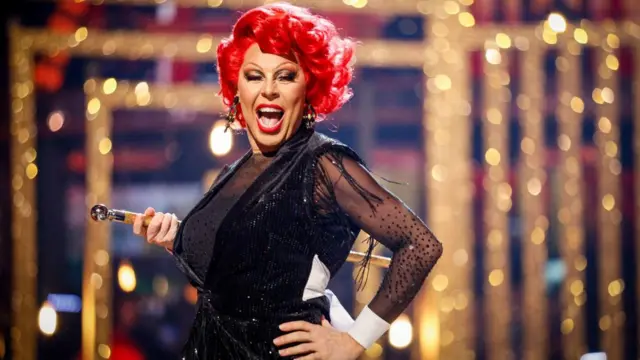 La Voix with her hand on her hip, dressed in black, on the Strictly dance floor