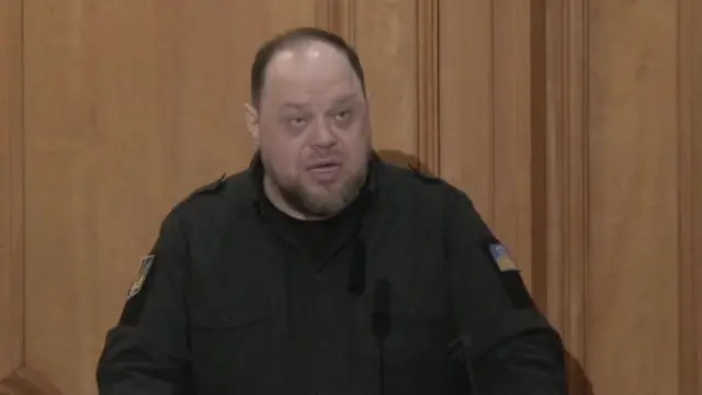 Man speaking in front of brown wall