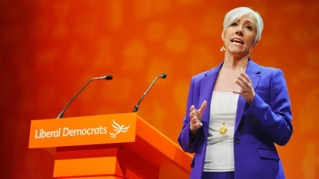 Deputy leader of the Liberal Democrats Daisy Cooper delivering keynote speech during the party's autumn conference, standing in front of an orange background and wearing a purple suit