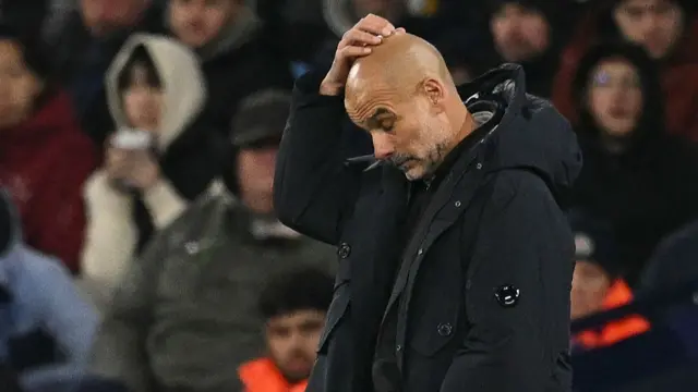 Pep Guardiola touches his head on the touchline