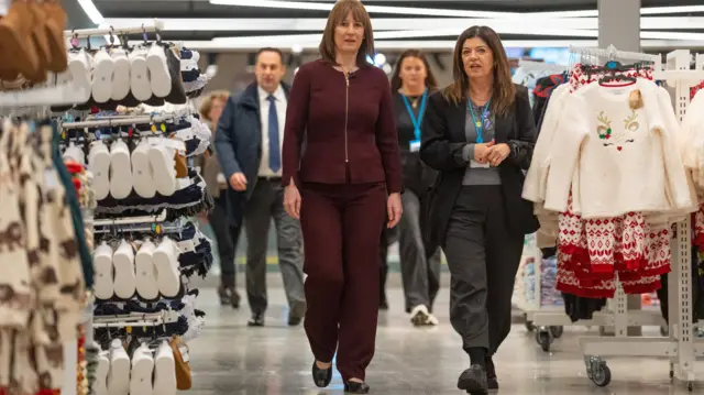 Rachel Reeves, wearing a red suit, walking through a clothes shop