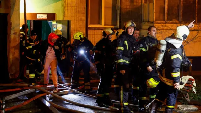 Firefighters assist a woman during an evacuation at the site of an apartment building