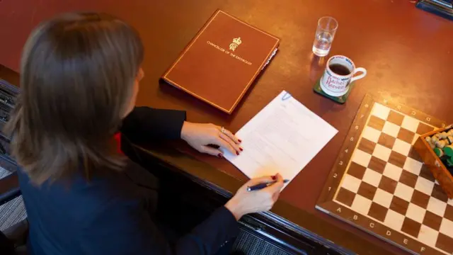 Aerial picture of Reeves looking at document on table with coffee cup and chess board next to her