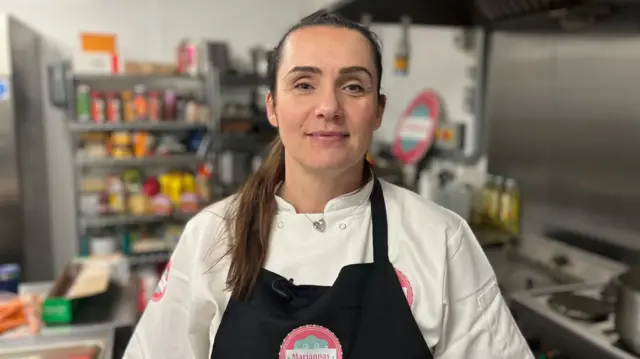 Marianna Penman in a kitchen stacked with food, wearing a pinny