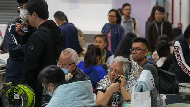 Geçici bir barınakta bulunan Hong Konglular, bazıları telefonla konuşuyor, bazıları ise battaniyelere sarılı