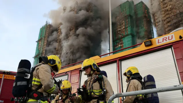 Firemen stand in front of  a van