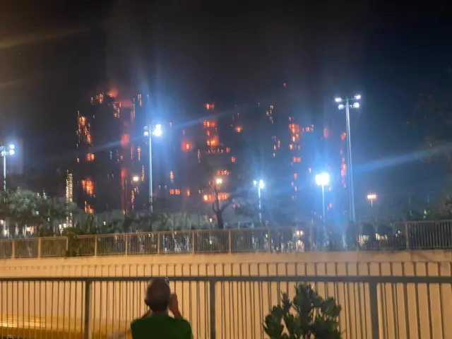 A blurry picture of a building block on fire in Hong Kong, a man taking pictures at the bottom of the frame