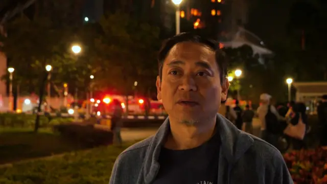 Jason Kong, a Hong Kong resident stands in front of the emergency workers battling the blaze at his apartment building