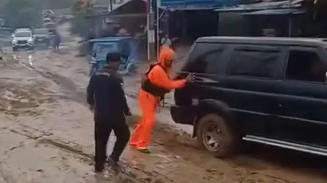 A man in orange waterproofs helps push a car out of thick post-flood mud near Sibolga, Indonesia