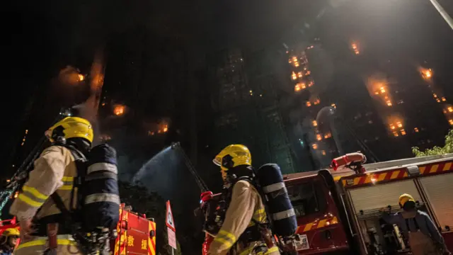 Fire fighters and engines at the base of the Hong Kong tower blocks on fire, at night