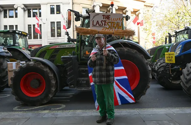 A man stood in front of a tractor holding a sign that says 