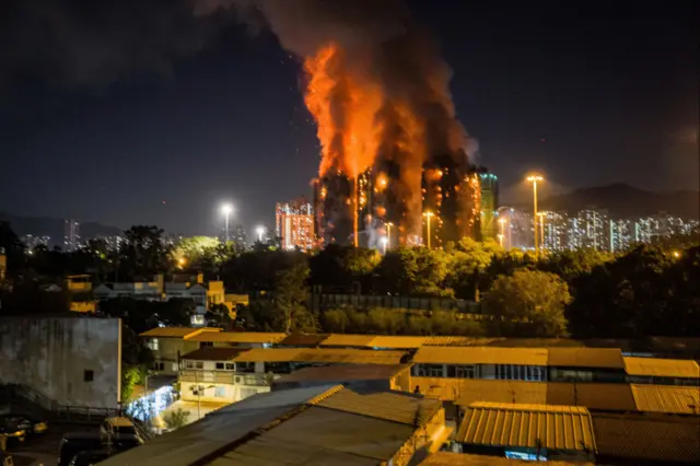 An eight-building block in flame, smoke billowing into the night sky with Hong Kong's skyline and mountains in the background