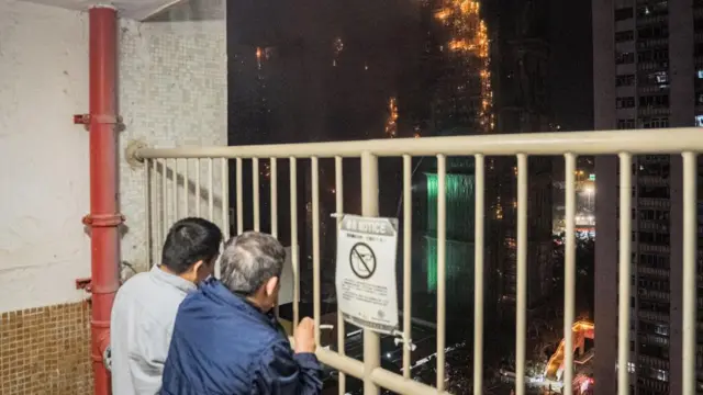 Two men watch the blaze through a metal grate from a nearby building.