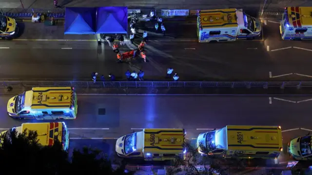 An aerial view of several ambulances lining a street, and emergency responders treating someone on a stretcher