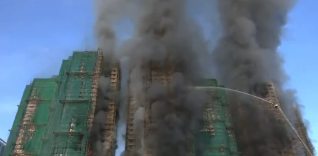 Smoke can be seen issuing from three of the blocks that are covered in bamboo scaffolding and green netting