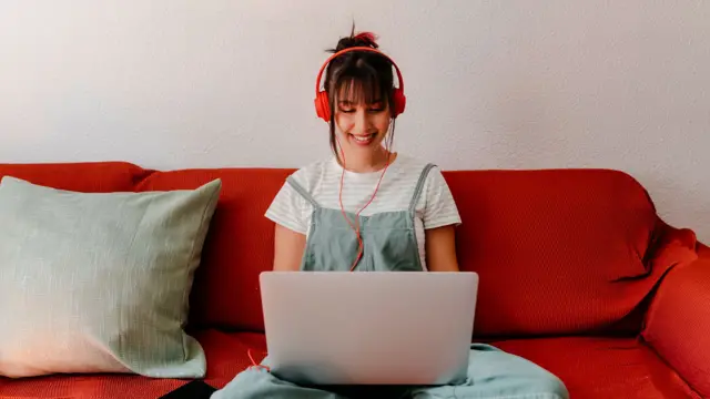 Woman wearing headphones sat on sofa with laptop on her lap