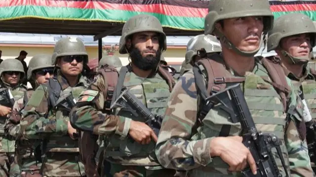 A row of men in military fatigues hold guns