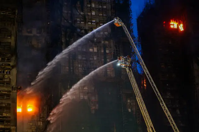 Fire crews use ladders to spray water on flames inside a Hong Kong tower block