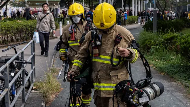 Firefighters walk near residential buildings that continue to burn at Wang Fuk Court in the Tai Po district