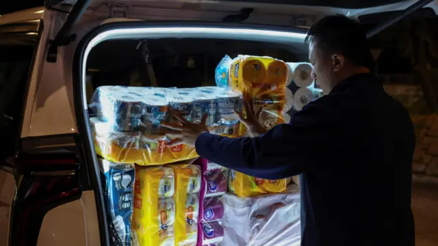 A man loads a car boot with supplies to take to the scene of the fire. He's lit up by the boot, everything else is in darkness.
