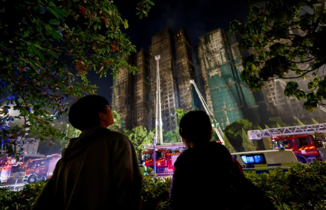 People stand near the scene of a deadly fire, which broke out yesterday at Wang Fuk Court housing comple