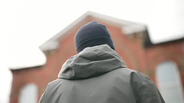 The back of a man wearing a grey coat and woolen hat