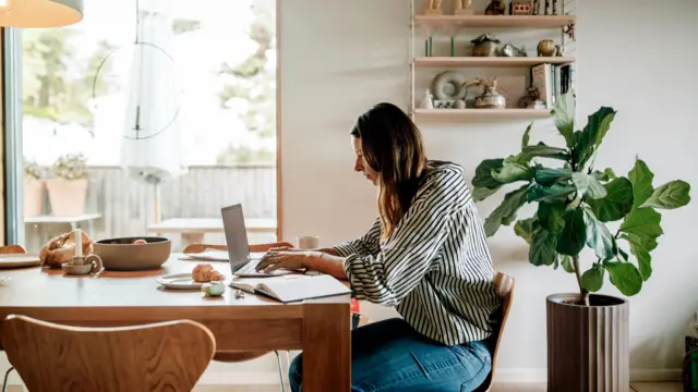 Woman in black and white striped shirt working on a laptop in home kitchen.