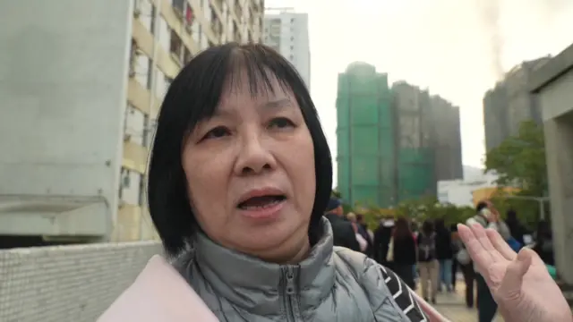 A woman stands outside the burning buildings. She's wearing a coat and talking to reporters. We can see crowds of people in the background