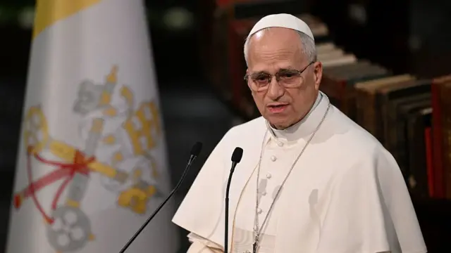 The Pope gives a speech in Turkey. He is dressed in white robes with a cross around his neck.
