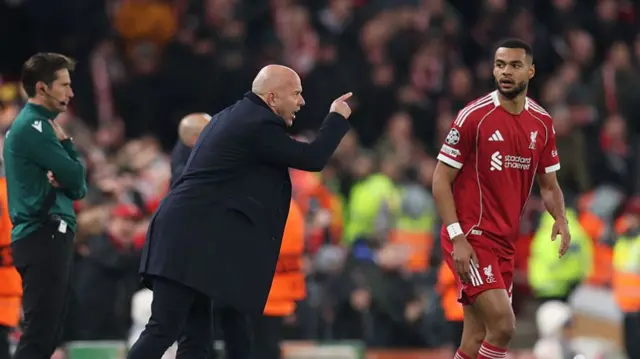Arne Slot gesturing towards his players on the touchline while Cody Gakpo stands on the pitch just to the side of him.