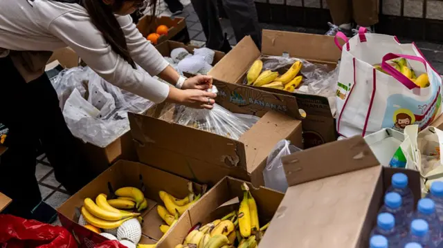 A woman unwraps food near residential buildings that continue to burn at Wang Fuk Court