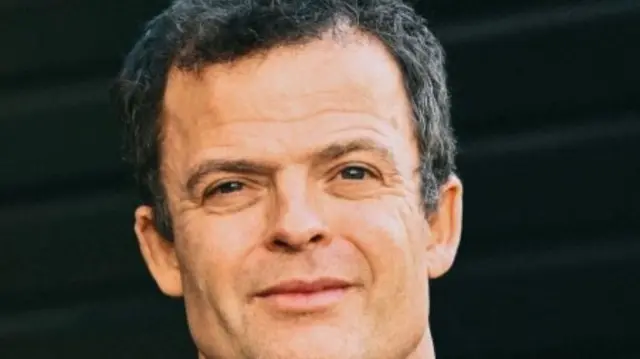 Thomas Powles looks at the camera with a neutral expression and black background