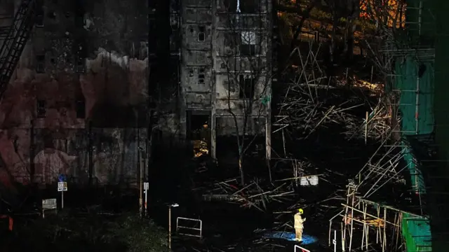 A lone firefighter stands at the site of the burnt apartment blocks in darkness