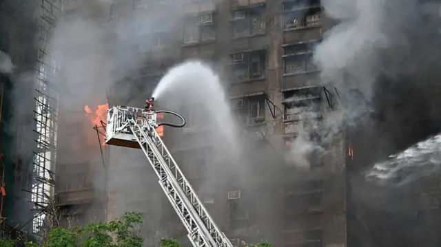 A firefighter on a crane sprays water on a burning building
