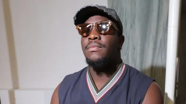 A man in a vest and cap with sunglasses on