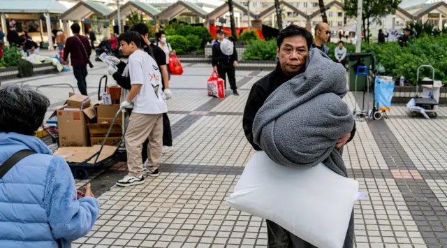 A man carring a blanket and pillow walking among volunteers handing out supplies